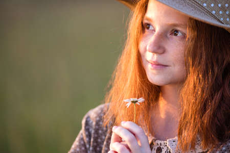 emotional redhead girl stands in the grass on a summer meadow at sunset in an elegant dressの写真素材