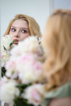 Indoor shot of beautiful girl holding white and rose peonies, winsome woman with big bouquet, enjoying her flowersの写真素材