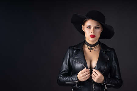 Woman in big black hat and jacket, studio portrait, dark backgroundの写真素材