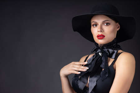 Woman in big black hat and jacket, studio portrait, dark backgroundの写真素材