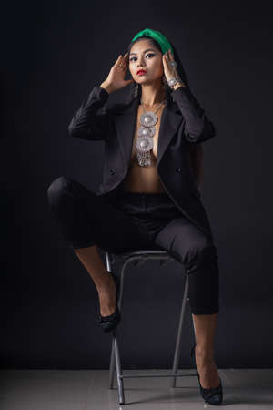 Woman in big black hat and jacket, studio portrait, dark backgroundの写真素材