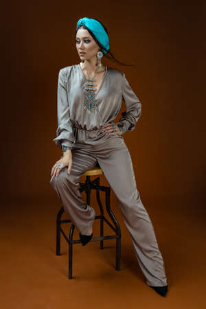 Glamor portrait of beautiful woman model with natural lips and long dark haid with silk jumpsuits and luxury jewelryの写真素材