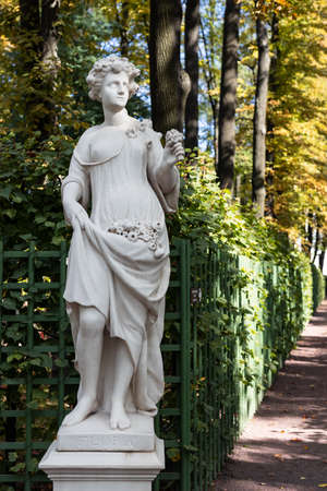 Old park statue of sensual Greek or Italian Renaissance Era woman with flowers in city park went to golden Autumn colors,の写真素材