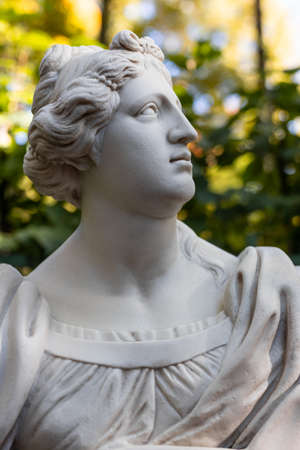 Old park statue of sensual Greek or Italian Renaissance Era woman with flowers in city park went to golden Autumn colors,の写真素材