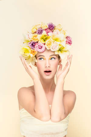 Studio portrait of a young girl with flowers instead of hairstyles, looks into the camera. Expression of surprise on the faceの写真素材