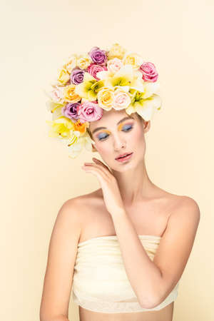 Studio portrait of a young girl with flowers instead of hairstyles, looks into the camera. On a gentle yellowish backgroundの写真素材