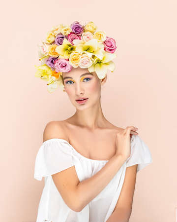Young beautiful woman with bouquet of flower in head. Art portrait of sexy blonde with colorful flowers. Professional art makeup. Pretty pink background. Happy conceptの写真素材