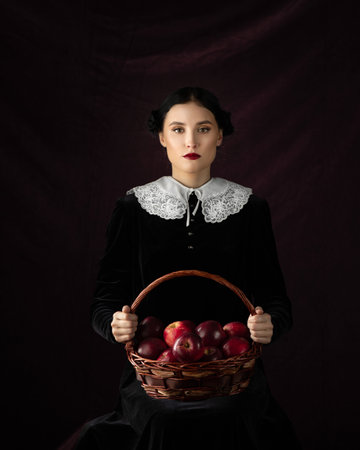 Model in gothic costume on a black background. The girl is holding a red apple as symbol of temptationの写真素材