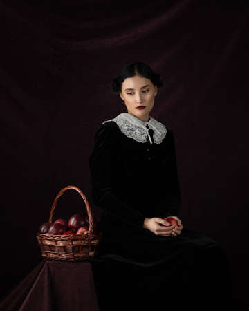 Studio portrait of pretty woman dark hair, white collar. Face, Thinking. Hold red apple. Dark...
