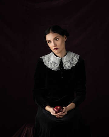 Girl in a historical dress sitting wirh red apple in hands. Studio portraitの写真素材
