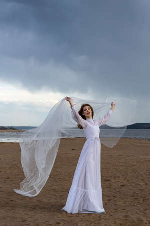 Happy young girl in a white dress on the river bank. Stormy sky in the cloudsの写真素材