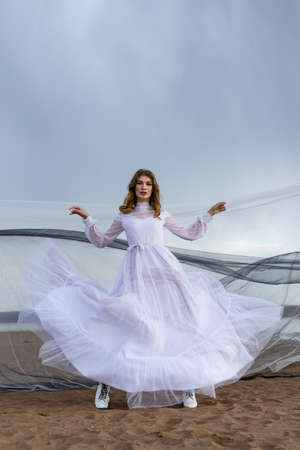 Happy young girl in a white dress has fun on the river bank. Stormy sky in the cloudsの写真素材
