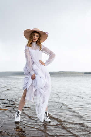 Happy young girl in a white dress has fun on the river bank. Stormy sky in the cloudsの写真素材