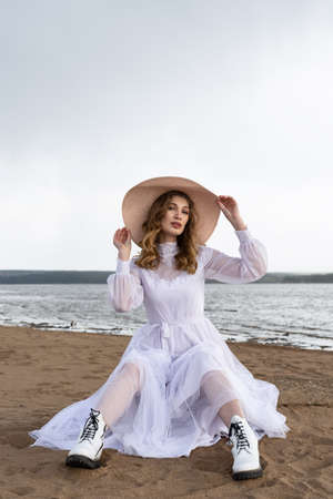 Happy young girl in a white dress has fun on the river bank. Stormy sky in the cloudsの写真素材