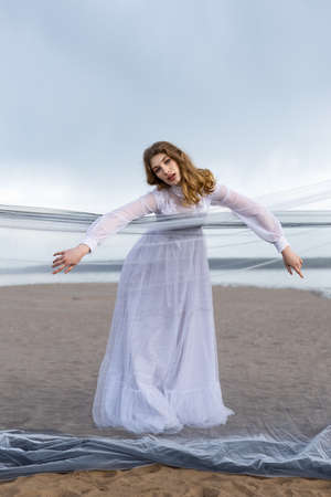 Happy young girl in a white dress has fun on the river bank. Stormy sky in the cloudsの写真素材