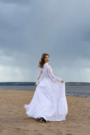 Happy young girl in a white dress on the sandy shore. Thunder skyの写真素材