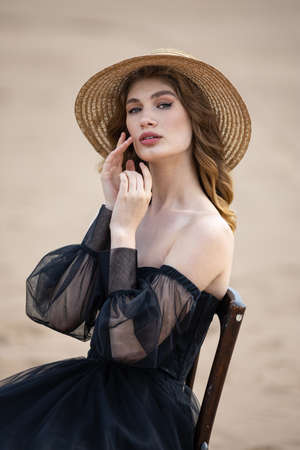 Happy young girl in a straw hat and in a black dress on the bank of the river. Thunder skyの写真素材
