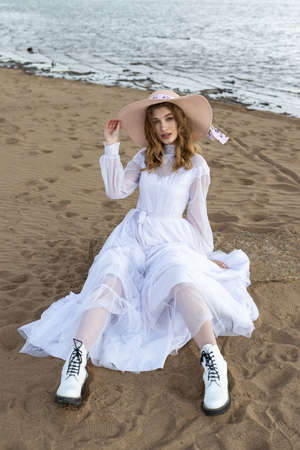 Happy young girl in a white dress has fun on the river bank. Stormy sky in the cloudsの写真素材