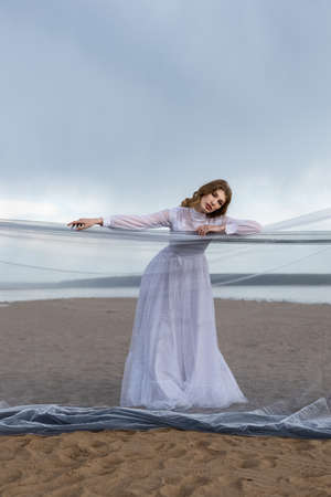 Happy young girl in a white dress has fun on the river bank. Stormy sky in the cloudsの写真素材