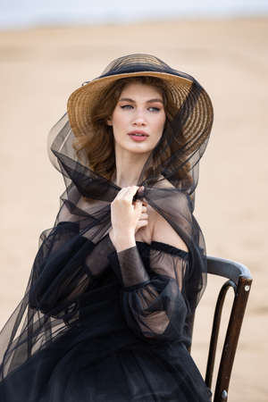 Happy young girl in a straw hat and in a black dress on the bank of the river. Thunder skyの写真素材