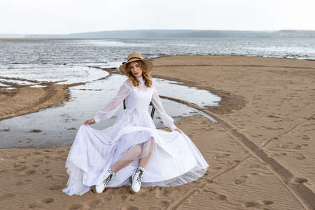 Happy young girl in a white dress on the river bank. Stormy sky in the cloudsの写真素材