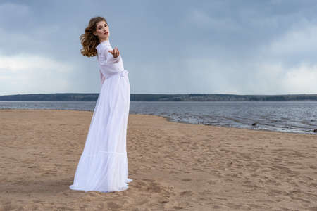 Happy young girl in a white dress on the river bank. Stormy sky in the cloudsの写真素材