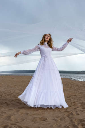 Happy young girl in a white dress on the sandy shore. Thunder skyの写真素材