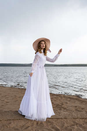 Happy young girl in a white dress on the river bank. Stormy sky in the cloudsの写真素材