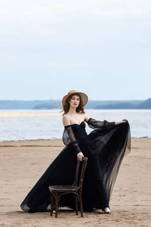 Happy young girl in a straw hat and in a black dress on the bank of the river. Thunder skyの写真素材