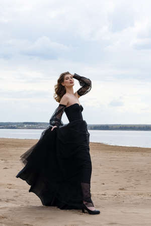 Happy young girl in a straw hat and in a black dress on the bank of the river. Thunder skyの写真素材