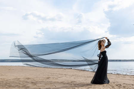 Happy young girl in a straw hat and in a black dress on the bank of the river. Thunder skyの写真素材