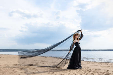 Happy young girl in a straw hat and in a black dress on the bank of the river. Thunder skyの写真素材