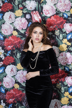 Beautiful model woman with curly hairstyle, background wall of flowersの写真素材