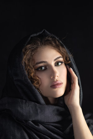 beautiful young woman with dark gray headscarf cover her face with luxury makeup on black background looking downの写真素材