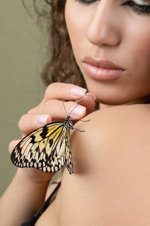 Beautiful young woman with perfect skin and bright yellow make up posing with butterfly on her face. beauty model with color professional makeup. SPA, wellness, make-up, skincare concept.の写真素材
