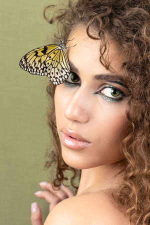 Fashion beauty model with butterfly on face and color professional makeup. SPA, wellness, make-up and skincare concept.の写真素材