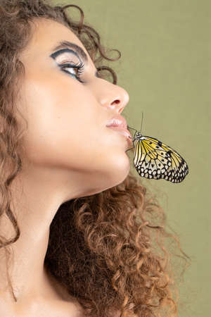 Beautiful young woman with perfect skin and bright yellow make up posing with butterfly on her face.の写真素材