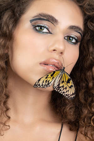 Beautiful young woman with perfect skin and bright yellow make up posing with butterfly on her face. beauty model with color professional makeup. SPA, wellness, make-up, skincare concept.の写真素材
