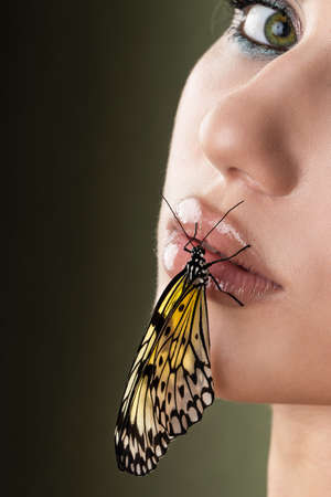 Beautiful young woman with perfect skin and bright yellow make up posing with butterfly on her face. beauty model with color professional makeup. SPA, wellness, make-up, skincare concept.の写真素材
