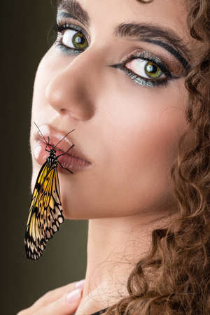 Beautiful young woman with perfect skin and bright yellow make up posing with butterfly on her face.の写真素材