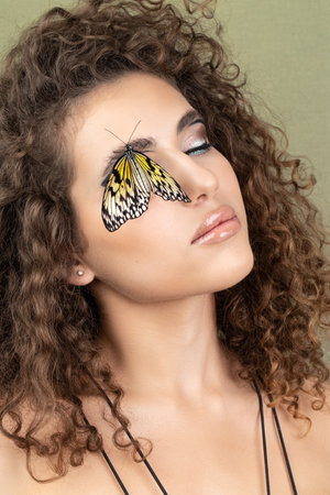 Beautiful young woman with perfect skin and bright yellow make up posing with butterfly on her face. beauty model with color professional makeup. SPA, wellness, make-up, skincare concept.の写真素材