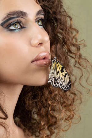 Beautiful young woman with perfect skin and bright yellow make up posing with butterfly on her face. beauty model with color professional makeup. SPA, wellness, make-up, skincare concept.の写真素材
