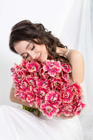 Sexy woman with flowers pink tulips in hands on a light backgroundの写真素材