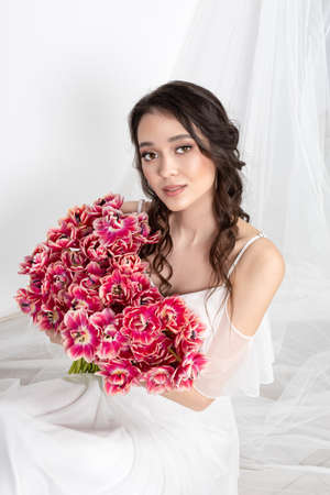 Young woman with pink tulips in hands, white dressの写真素材