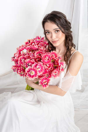 Young woman with pink tulips in hands, white dressの写真素材