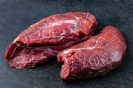 Fresh and raw fillet meat. Whole piece of beef tenderloin steaks set on black stone table background, no decorationの写真素材