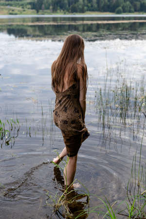 young fashionable woman standing in water on the lake beach at sunsetの写真素材