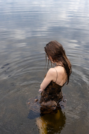young fashionable woman standing in water on the lake beach at sunsetの写真素材
