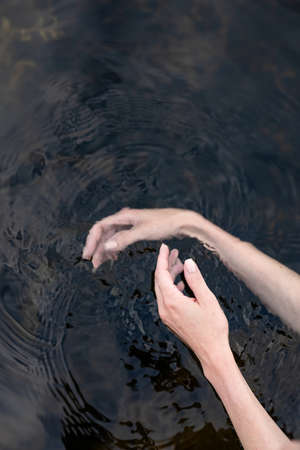 woman's hand gently touches the water in the pond, a close horizontal photo on the theme of tranquilityの写真素材