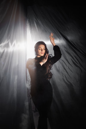 Pretty beautiful girl standing, posing, holding black curtains in her hands and playing with them. fashion studio portraitの写真素材